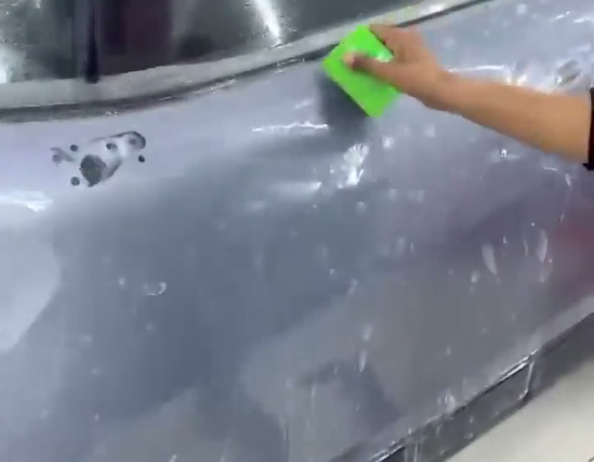 Roadster technician squeegeeing paint protection film onto a car door